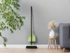 A broom and dustpan set stands against a gray wall next to a plant and a stool with a vase. Náhled obrázku produktu