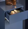 A close-up view of an open drawer in a blue cabinet, revealing a clear organizer containing bath brushes and a wooden-lidded jar. Náhled obrázku produktu