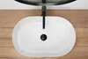 A top-down view of a white oval basin with a black faucet and drain, set against a wooden background. Náhľad obrázku produktu