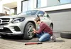 A man is changing a car tire in front of a garage. Náhľad obrázku produktu