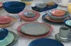 A collection of ceramic tableware, including bowls and plates, arranged on a textured surface. Produktbild-Vorschau