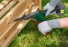 Hands wearing protective gloves are using a belt sander on a wooden structure outdoors. Produktbild-Vorschau