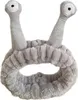 A grey cosmetic headband with two antennae-like protrusions on top, each with an eye design. Produktbild-Vorschau