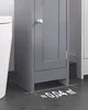 A close-up view of a gray bathroom cabinet next to a white toilet, with a measurement overlay on the floor. Podgląd zdjęcia produktu