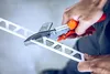 A person's hands are using a pair of orange-handled shears to cut a white metal strip. Anteprima dell’immagine prodotto