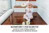 A baby sitting on a wooden floor with flowers, next to a white padded bumper. Produktbild-Vorschau