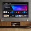 A large smart TV displaying various streaming service logos and movie posters, mounted on a concrete wall above a wooden media console. Produktbild-Vorschau