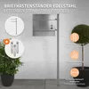 A stainless steel letterbox stand with a mailbox is shown in an outdoor setting, next to plants and a wall. Náhled obrázku produktu