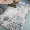 A rug is placed on a floor next to a sofa and an ottoman. Produktbild-Vorschau