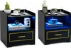 Two black nightstands with gold trim and blue LED lighting are displayed side-by-side against a white background. Each nightstand has a drawer and an open shelf with decorative items. Náhled obrázku produktu