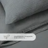 A close-up view of dark gray musselin bedding, showing the texture and a detail of a leaf icon with text. Produktbild-Vorschau