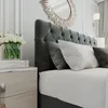 A close-up view of a bedroom setting, focusing on a bed with a tufted headboard, pillows, and a nightstand with flowers. Produktbild-Vorschau