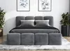 A bed with a gray upholstered headboard and frame, dressed with gray bedding and pillows. Four matching gray ottomans are placed at the foot of the bed. Two framed botanical prints hang on the wall above the headboard, and two potted plants flank the bed. Produktbild-Vorschau