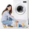 A woman is crouching next to a washing machine, reaching into a basket of laundry supplies. Produktbild-Vorschau