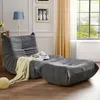 A gray beanbag chair and ottoman are set up in a living room with a lamp and artwork on the wall, next to a window with curtains.