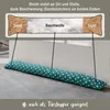 A draft excluder with a diagram showing its internal composition of sand and cotton, placed in front of a door. Produktbild-Vorschau