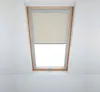 A skylight window with a beige roller blind partially lowered. Produktbild-Vorschau