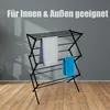 A black drying rack with two towels hanging on it, placed on a wooden floor in front of a gray wall. Produktbild-Vorschau