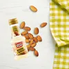 A small bottle of almond extract surrounded by almonds on a white wooden surface, with a green and white checkered cloth in the background. Voir les images du produit