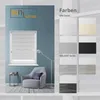 A room scene with a window featuring a roller blind, a chair, and a lamp, alongside a display of color swatches for roller blinds. Produktbild-Vorschau