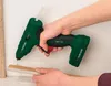 A person is using a cordless hot glue gun to apply glue to a piece of wood. Produktbild-Vorschau