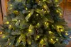 A close-up view of a green artificial Christmas tree with yellow LED lights. Produktbild-Vorschau
