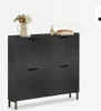 A black shoe cabinet with four flip-out compartments and metal legs, decorated with a vase of flowers and books on top.