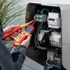 An electrician is testing electrical components inside a metal enclosure with two handheld testing devices. Náhľad obrázku produktu