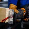 A person wearing work gloves is using a reciprocating saw to cut through a piece of wood and metal. Voir les images du produit