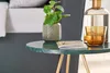 A close-up of a small round side table with a plant, a book, and a glass of amber liquid. Produktbild-Vorschau