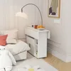 A white folding table next to a sofa with pillows, a floor lamp, and a framed picture on the wall. Voir les images du produit