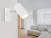 A white spotlight fixture mounted on a textured wall in a modern living room with a sofa and sheer curtains in the background. Produktbild-Vorschau