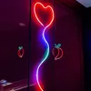 A neon heart-shaped light with a wavy stem, accompanied by neon fruit shapes, displayed against a dark, reflective background. Produktbild-Vorschau