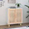 A white sideboard with natural rattan doors and wooden legs is placed against a light gray wall. Náhled obrázku produktu