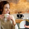 A woman is holding a cup of coffee, with a graphic of a coffee cup and a close-up of a red button on a white appliance in the foreground. Anteprima dell’immagine prodotto