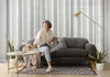 A woman sits on a sofa, holding a tablet and a cup, in a living room with curtains and a floor lamp. Voir les images du produit