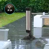 A black vertical infrared heater is shown on a wet outdoor patio next to outdoor furniture and a white cube-shaped side table. Lush green bushes are in the background. Anteprima dell’immagine prodotto