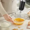 A person is using a hand blender to whisk eggs in a glass bowl, with ingredients like flour and eggs nearby. Anteprima dell’immagine prodotto
