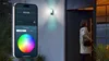 A woman is opening a door while a smartphone displays controls for a smart home camera with a color wheel. Anteprima dell’immagine prodotto