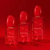 Three red perfume bottles of varying sizes are arranged in a row against a solid red background. Podgląd zdjęcia produktu
