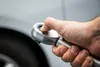 A hand is holding a torque wrench, with a car tire and body in the background. Anteprima dell’immagine prodotto