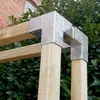 A close-up view of metal corner brackets connecting wooden posts and beams, with greenery and a brick wall in the background. Produktbild-Vorschau