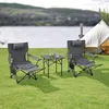 Two camping chairs and a small table are set up on a grassy area next to a lake, with a tent in the background. Náhled obrázku produktu