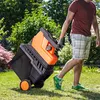 A person is pulling a garden shredder across a lawn in a garden. Produktbild-Vorschau