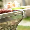 A close-up of a portable barbecue grill with a hamburger patty on it, set outdoors. Produktbild-Vorschau