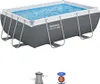 A rectangular above-ground swimming pool filled with blue water, supported by a metal frame. Below the pool are two accessories: a water filter pump and a filter cartridge. Produktbild-Vorschau