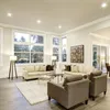 A spacious and well-lit living room with large windows, sofas, armchairs, and coffee tables. Voir les images du produit