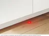 A close-up view of a red light on a wooden floor near a white cabinet baseboard. Produktbild-Vorschau