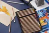 A set of colored pencils is laid out on a blue surface next to a drawing of a fox and a patterned fabric. Produktbild-Vorschau