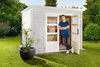 A man stands in the doorway of a white wooden shed in a garden. Produktbild-Vorschau